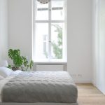 A bedroom with white walls, crown molding, light gray bedding