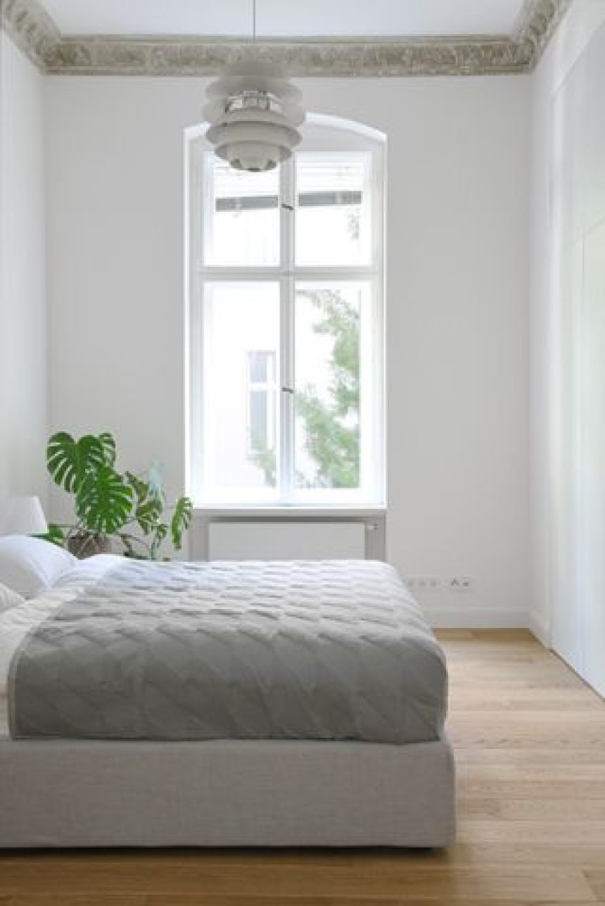 A bedroom with white walls, crown molding, light gray bedding