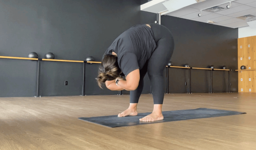 Yoga teacher standing in a forward bend on a yoga mat.