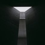 still from The Brutalist with light pouring into dark room through triangular skylight into shaft below