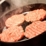 Four hamburgers in a hot frying pan.