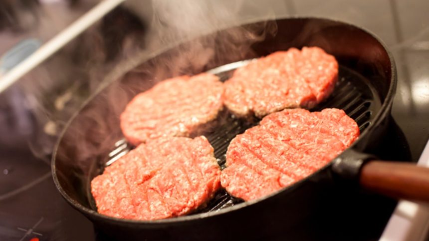 Four hamburgers in a hot frying pan.