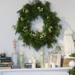 green wreath above white fireplace mantel lined with candlesticks photo frames books