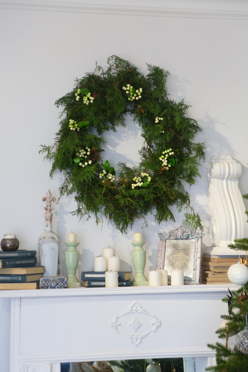 green wreath above white fireplace mantel lined with candlesticks photo frames books