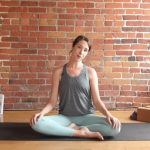 Kassandra Reinhardt teaching a 10-minute morning yoga session while seated and tilting her head and neck to one side during a full-body stretching routine