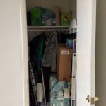 Image of an open small closet that is full of cleaning supplies, jackets, toilet paper, and a mix of random house items.