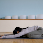 Yoga teacher on a mat practicing Child's Pose with her knees wide and toes touching