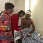 An injured man sits in a hospital bed with a thick bandage around his head as he is examined by a doctor.