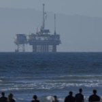 An offshore oil rig is seen as a group of people help clean the beach in Huntington Beach, California, U.S., November 14, 2024. — Reuters