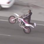 A dirt bike rider doing a wheelie on the highway in California