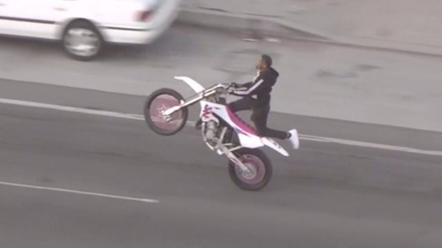 A dirt bike rider doing a wheelie on the highway in California