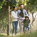 Young man and woman enjoying a walk in a park while their daughters rides on a bike infront of them