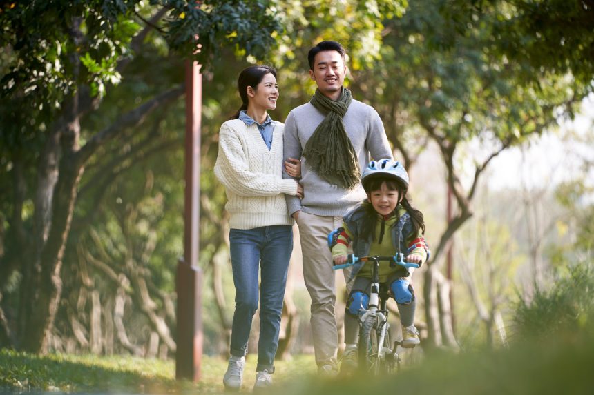 Young man and woman enjoying a walk in a park while their daughters rides on a bike infront of them