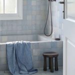 blue tiled bathroom with blue denim colored towel draped over the bath, timber stool beside