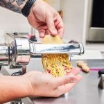 Hands guiding dough through Marcato Atlas 150 Pasta Machine as it cuts noodles