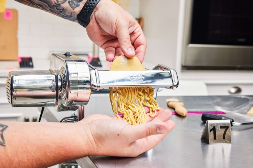 Hands guiding dough through Marcato Atlas 150 Pasta Machine as it cuts noodles