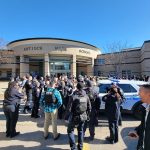 A crowd of civilians and police officers gathers outside of Antioch High School.