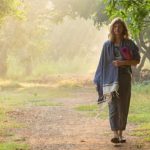 woman walking through a grove of trees with a pink yoga mat rolled under her arm at a wellness retreat