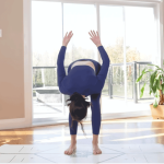 Woman practicing on a yoga mat folding forward and sweeping her arms behind her