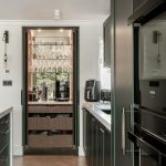 Dark green kitchen with a pocket door breakfast bar area with wooden drawers and glass shelves within