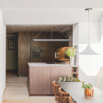 A pale dining area leading to a dark, wood cladded kitchen