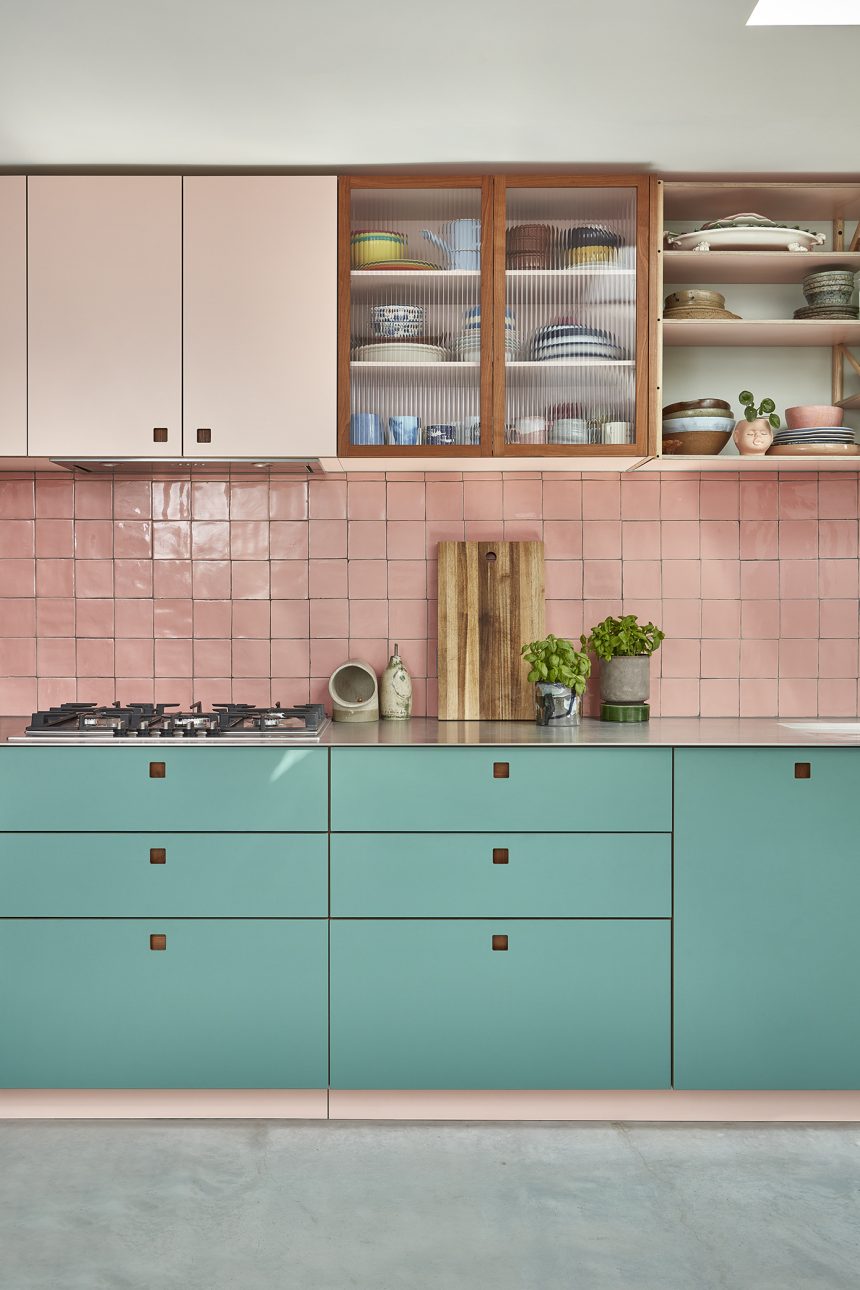 Bright light blue lower kitchen cabinets with bright pink kitchen cabinets above. Glass cabinets have also been integrated within the design, adding a seamless touch to the space. Baby pink zellige tiles have been used for the splashback.