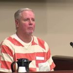 Colin Gray wearing an orange-and-white jumpsuit in court