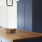 A blue painted shaker with a wooden countertop. A fruit bowl also sits atop the counter.