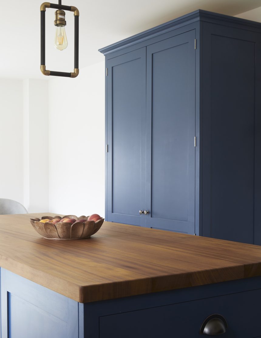 A blue painted shaker with a wooden countertop. A fruit bowl also sits atop the counter.