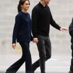 Meghan Markle wears a navy sweater, black bootcut jeans, and black boots while walking with Prince Harry