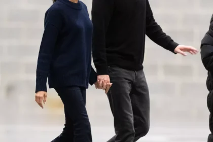 Meghan Markle wears a navy sweater, black bootcut jeans, and black boots while walking with Prince Harry