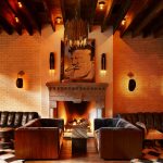 Lobby at the Ludlow Hotel in NYC with several leather couches warm lighting and a large portrait over a fireplace.