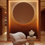 A golden-glowing modernly designed spa features whimsical furnishings including a white shearling armchair and a sun-like wall installation.