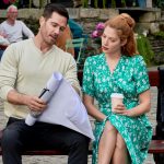 Luke Macfarlane left holding blueprints sitting on park bench beside Rachelle Lefevre in the Hallmark romantic comedy...